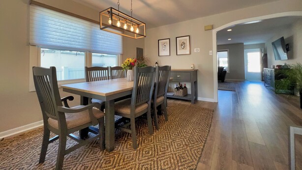 A dining area with a wooden table, four chairs, a patterned rug, and a hanging light fixture.