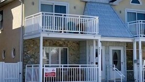 A two-story house with a balcony on the upper floor, a stone facade, and a 'For Sale' sign.