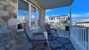 A stone exterior with a balcony, two Adirondack chairs, and a patterned rug.