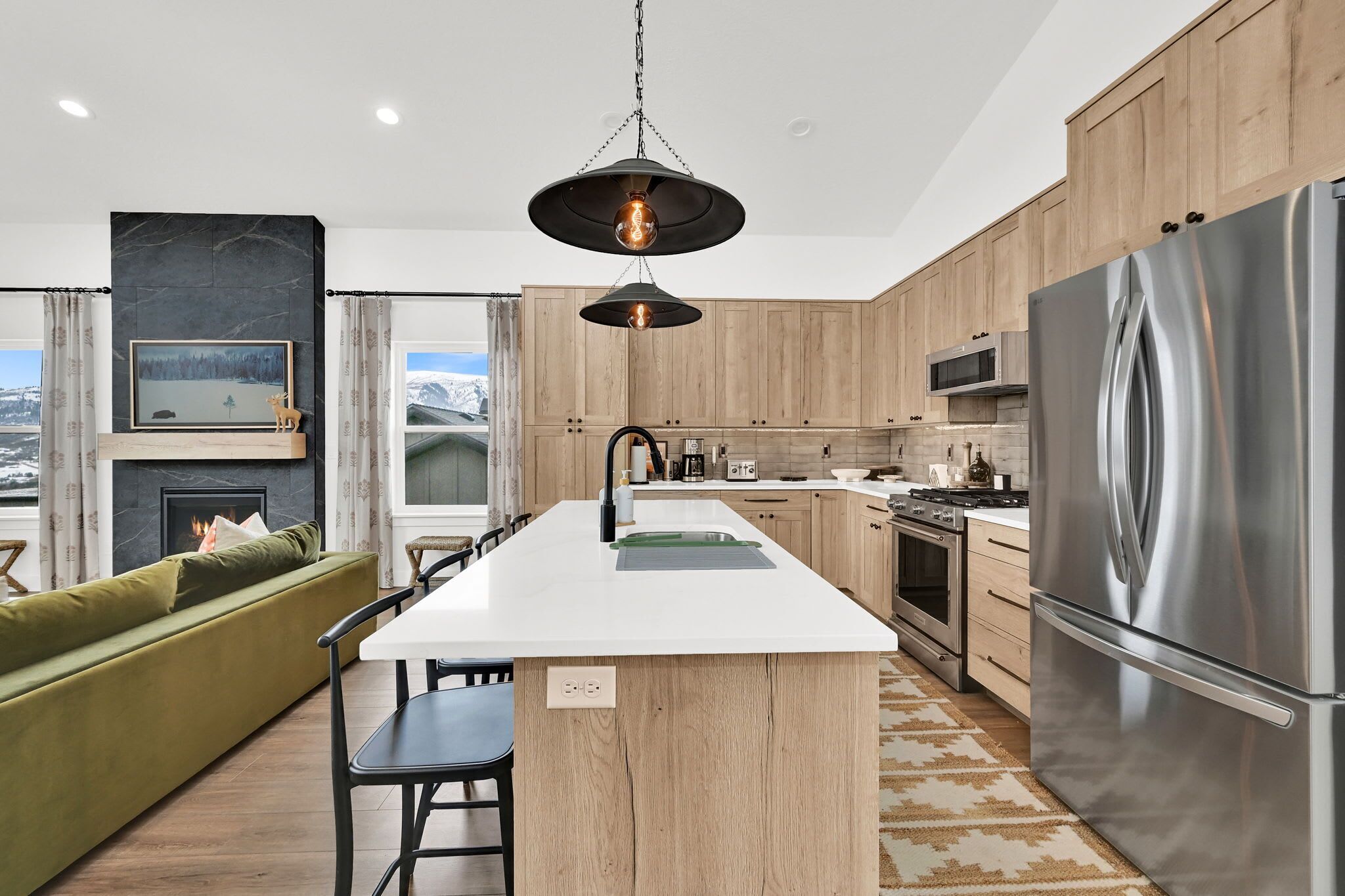 Une cuisine moderne dotée d’un îlot central, de meubles en bois, d’appareils électroménagers en acier inoxydable et d’une cheminée.