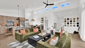 A spacious living area with a kitchen, a ceiling fan, and a wall displaying various hats. - Eden House: Ski Retreat w/ Hot Tub & Views (Eden)