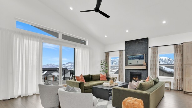 A modern living room with a fireplace, large windows, and a view of snow-capped mountains. - Eden House: Ski Retreat w/ Hot Tub & Views (Eden)