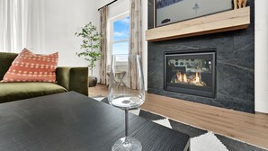 A living room with a fireplace, a glass of wine on a table, and a green sofa with a patterned pillow. - Eden House: Ski Retreat w/ Hot Tub & Views (Eden)