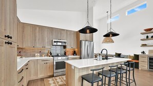 A modern kitchen with wooden cabinets, stainless steel appliances, and a central island with bar stools. - Eden House: Ski Retreat w/ Hot Tub & Views (Eden)