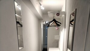 A narrow hallway with white walls, black flooring, and a mirror on the right. There are hanging clothes on a rack and a door at the end. - Imperial suite COLOSSEUM (Roma)