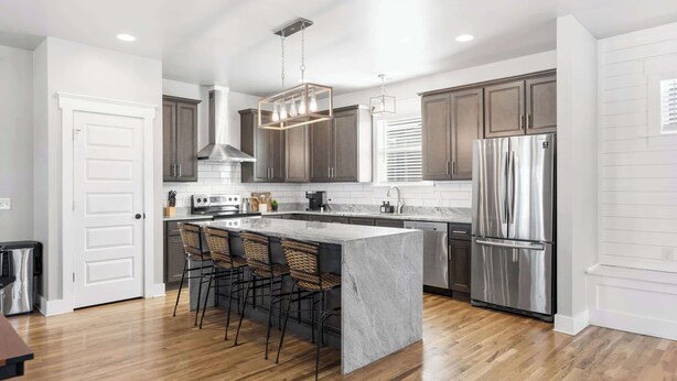A modern kitchen with dark wooden cabinets, stainless steel appliances, and a central island with bar stools. - Lucky Bachelor 5 Min to Broadway (Nashville)