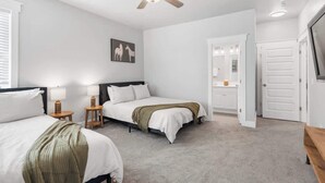 A bedroom with two beds, a ceiling fan, a bedside table with a lamp, a framed picture on the wall, and a door leading to another room. - Lucky Bachelor 5 Min to Broadway (Nashville)