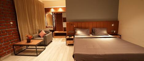 A modern hotel room with a large bed, a sofa, a small table, and a brick wall.