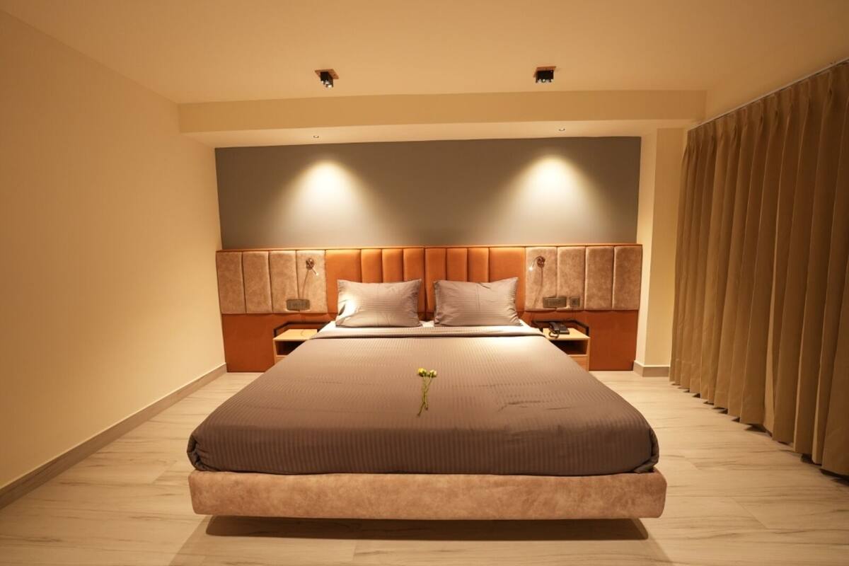 Ein modernes Hotelzimmer mit einem großen Bett, einem Holz-Kopfstück, Nachttischen und einem Vorhang auf der rechten Seite.