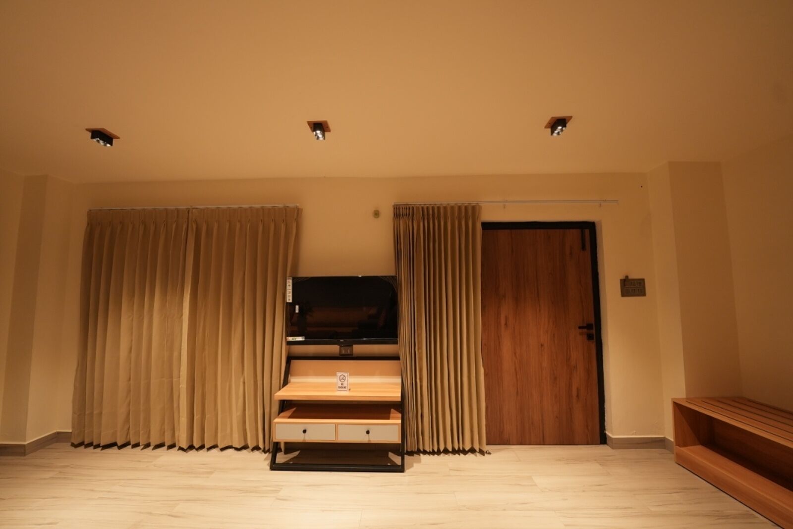 Una habitación con un banco de madera, un televisor sobre un mueble y una puerta.