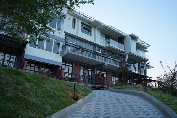 A multi-story residential building with a brick facade, large windows, and a covered outdoor area. - AURA CRIMSON VISTAS (Kodaikanal)