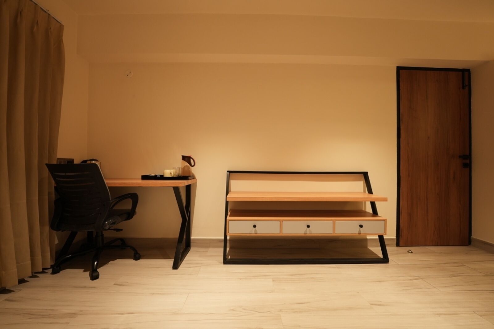 Una stanza con una scrivania in legno, una sedia da ufficio nera, una struttura letto in legno e una porta in legno.