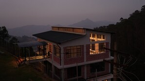 Une maison à deux étages dotée d’un balcon, de grandes fenêtres et offrant une vue sur les montagnes en arrière-plan.