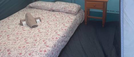 Een tent met een bed, een klein houten tafeltje en een muur met gedeeltelijk uitzicht op een stadslandschap.