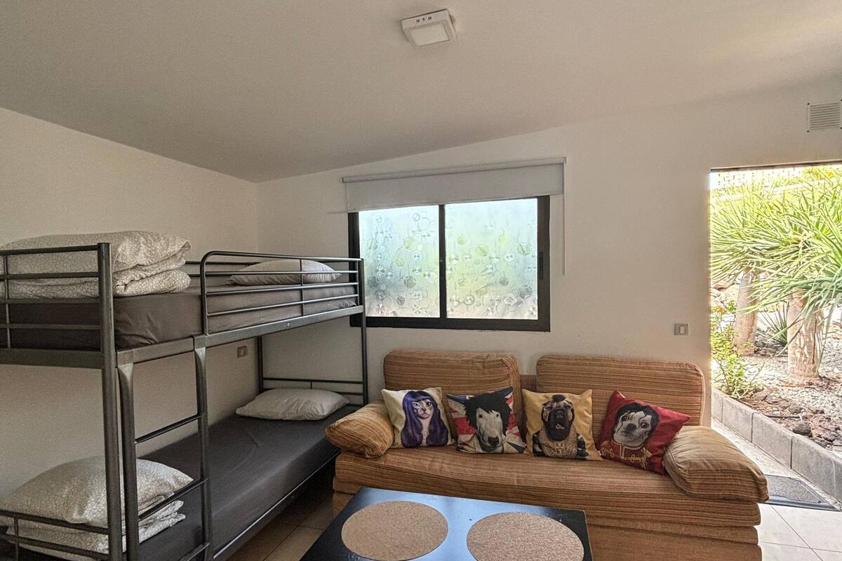 A dorm-style room with bunk beds, a sofa with decorative pillows, and a small table.