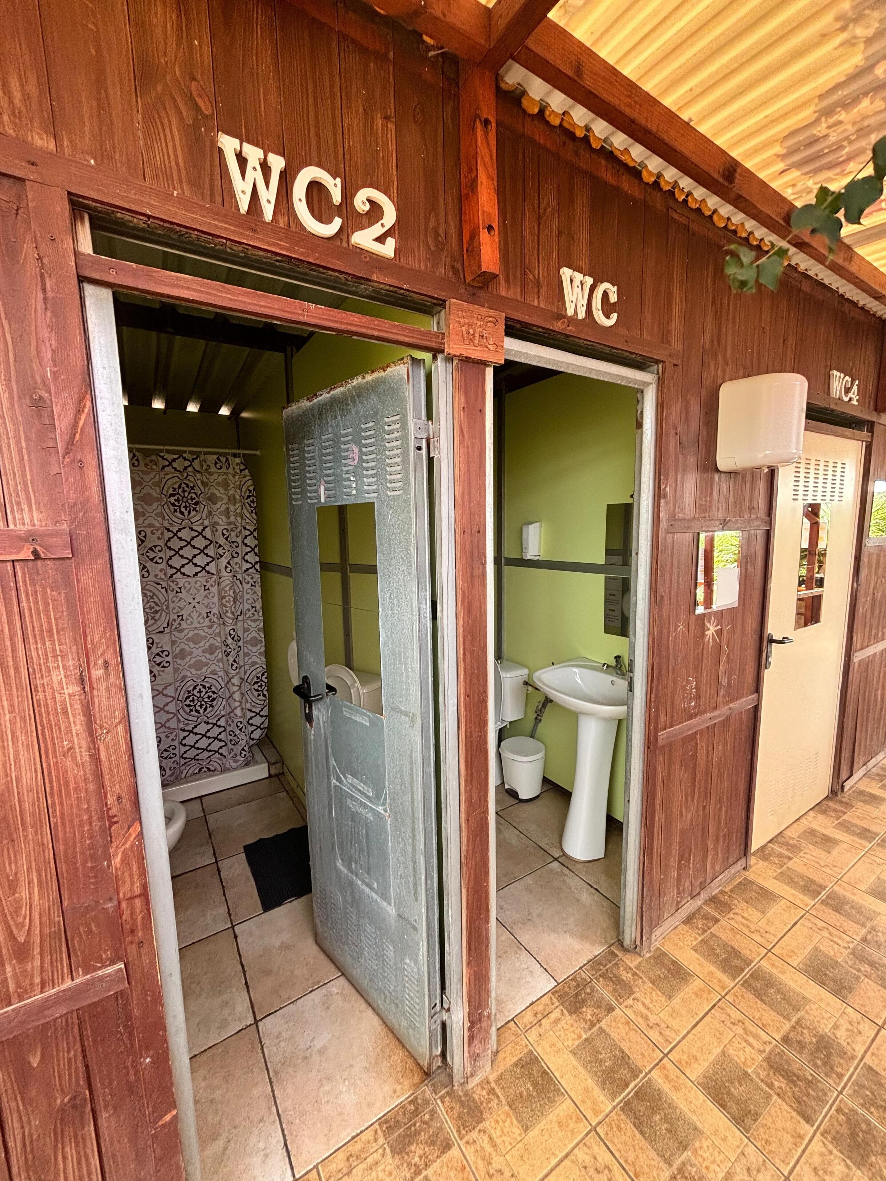 Edificio de madera con dos puertas identificadas, una con la etiqueta WC2 y otra con WC, que conducen a baños separados.