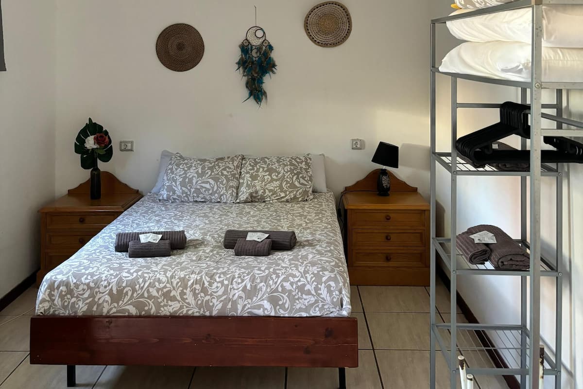 A bedroom with a bed, wooden nightstands, a wall-mounted shelf, and a bunk bed.