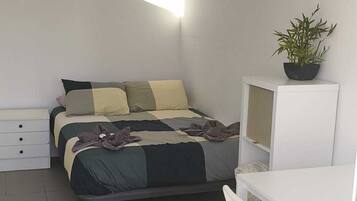 Een kleine, moderne slaapkamer met een bed, een bureau, een stoel en een kamerplant.