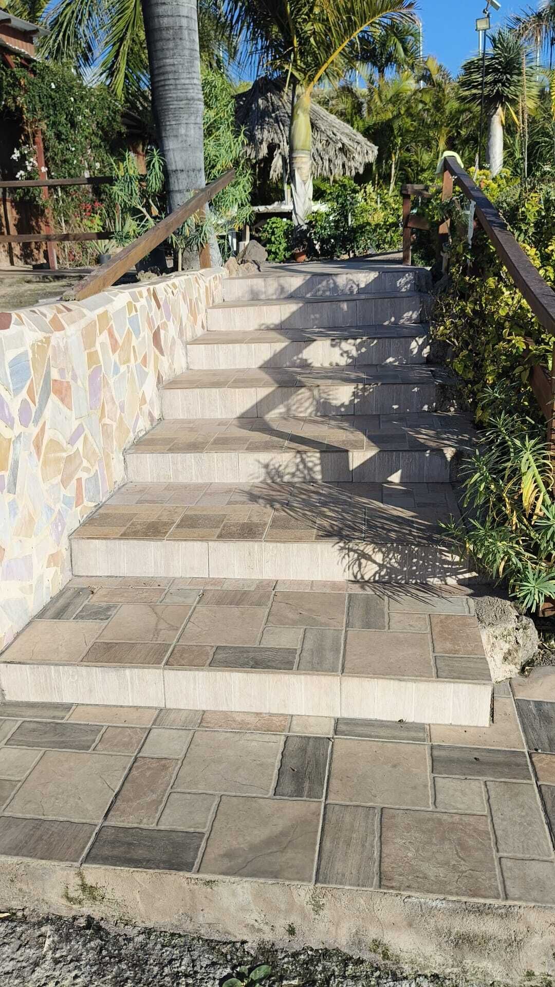 A set of stone steps leading up to a building with a thatched roof, surrounded by tropical vegetation.