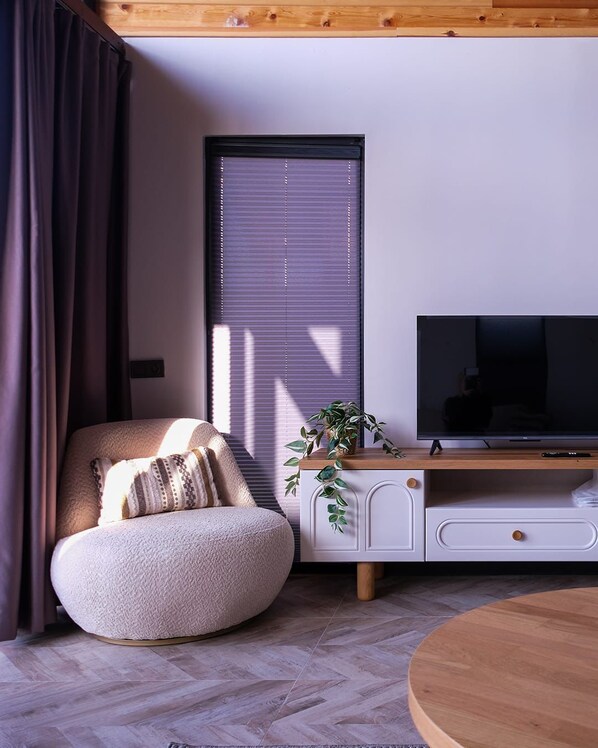 A modern living room with a round seating area, a television on a wooden stand, and a window with blinds. - Bell Garden Maşukiye (Kartepe)