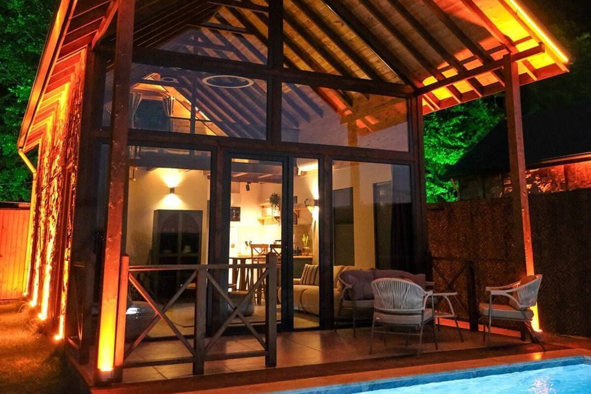 A modern house with a glass facade, a covered patio, and a swimming pool.