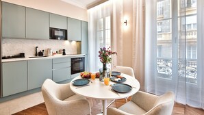 A modern kitchen with light blue cabinets, a white dining table with four chairs, and a large window with sheer curtains. - Aparthotel 9 ALBERTI Nice Centre (Nice)