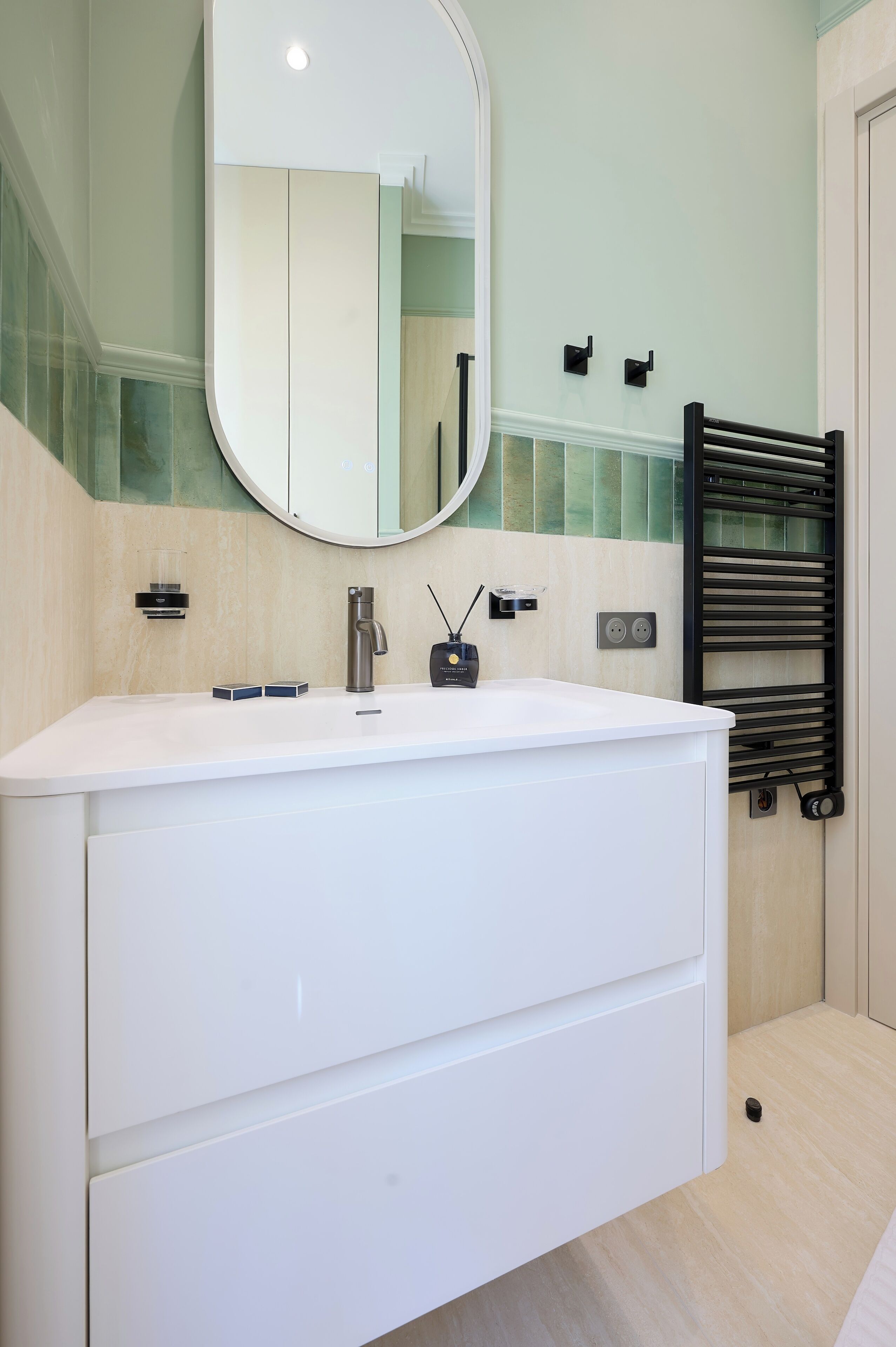 A modern bathroom with a white vanity, a round mirror, and a towel rack.