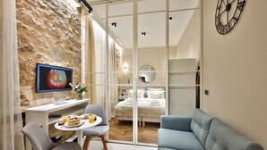 Una moderna camera d'hotel con parete in pietra, televisore, zona pranzo con tavolo e sedie, letto con lenzuola bianche e divano blu.