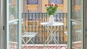 Un balcone con tavolo e sedie, una pianta in vaso e vista su un edificio giallo con balconi.