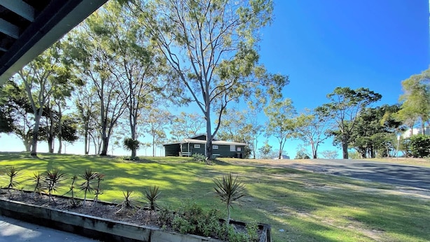 A residential property with a well-maintained lawn, a small house, and surrounding trees. - Burrum River Unit One (Burrum Heads)