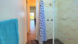 A bathroom with a shower curtain, tiled walls, and a visible door leading to another room. - Burrum River Unit One (Burrum Heads)
