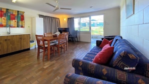 A spacious living area with a wooden dining table, chairs, a sofa, and a ceiling fan. - Burrum River Unit One (Burrum Heads)
