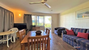 A dining area with a table and chairs, a ceiling fan, a sofa, and a window with curtains. - Burrum River Unit One (Burrum Heads)