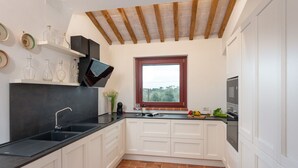 Una cocina con armarios blancos, encimera negra, ventana con vistas y suelo de ladrillo.