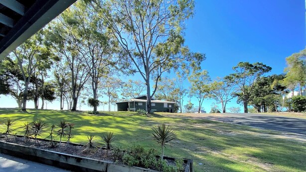 A residential property with a well-maintained lawn, a small house, and surrounding trees.
