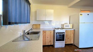 A compact kitchen with a sink, wooden cabinets, a microwave, a stove, and a refrigerator.