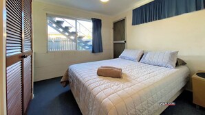 A bedroom with a bed, a ceiling fan, a window with curtains, and a door with blinds.