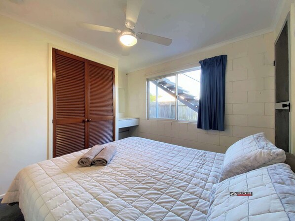 A bedroom with a bed, a ceiling fan, a window with curtains, and a wooden door. - Burrum River Unit Two (Burrum Heads)