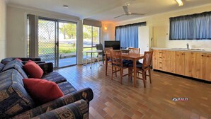 A spacious living area with a sofa, dining table, and chairs. There is a kitchen area with a sink and cabinets.