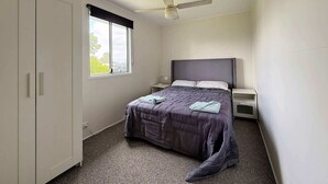 Une chambre à coucher comprenant un lit, une table de chevet, une armoire, une fenêtre avec vue et un ventilateur de plafond.