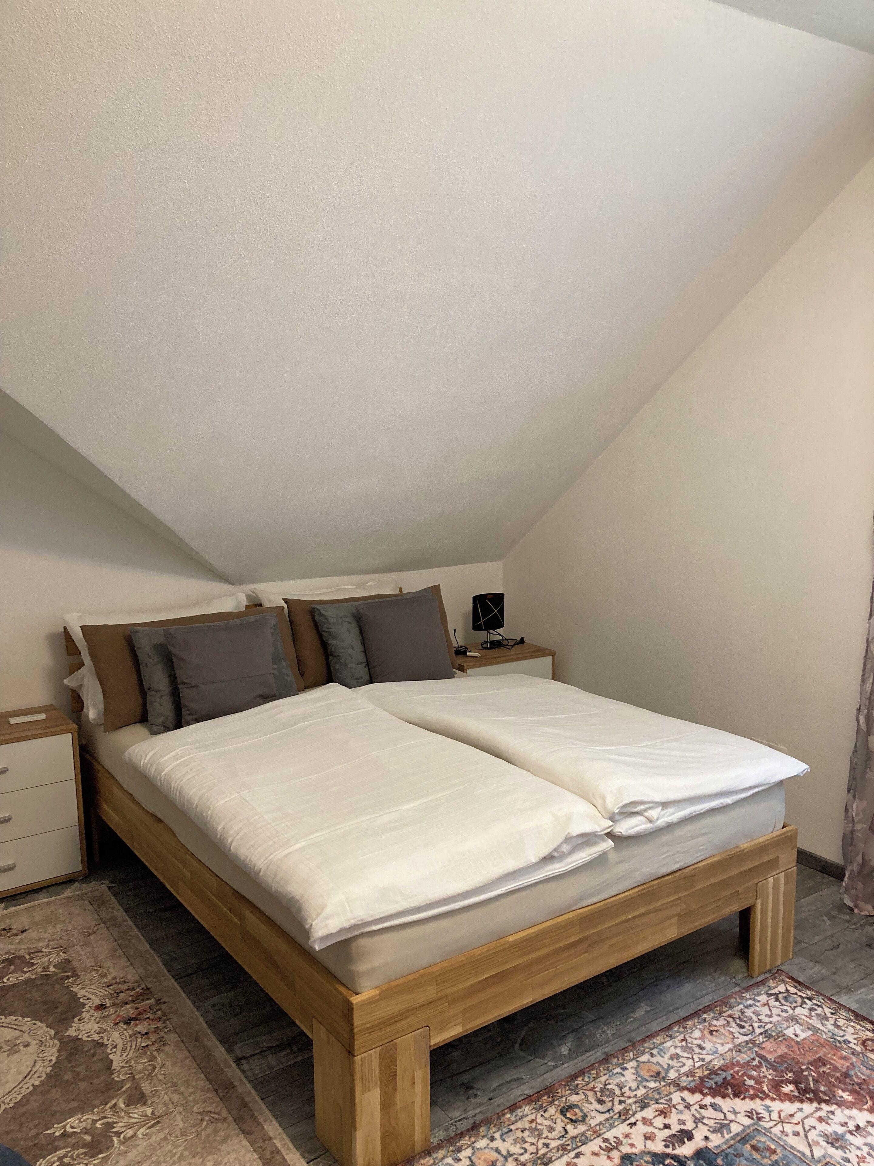 A bedroom with a wooden bed, a nightstand, and a patterned rug.