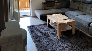 Ett modernt vardagsrum med en hörnsoffa, ett litet träbord och en mörk, lurvig matta.