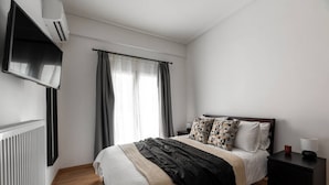 A modern bedroom with a bed, a nightstand, a TV mounted on the wall, and a window with curtains. - Urban Chic Hideaway Near Athens Center & Metro (Athina)