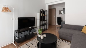 A modern living room with a flat-screen TV, a black entertainment unit, a grey sofa, and a small round coffee table. - Urban Chic Hideaway Near Athens Center & Metro (Athina)