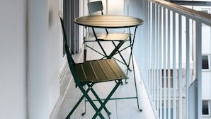 A balcony with a table and chairs, a window, and an air conditioning unit. - Urban Chic Hideaway Near Athens Center & Metro (Athina)