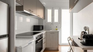 A modern kitchen with white cabinetry, a black induction cooktop, a microwave, a sink with a faucet, and a coffee maker. - Urban Chic Hideaway Near Athens Center & Metro (Athina)