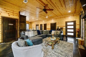 A spacious living room with a sectional sofa, a coffee table, and a ceiling fan. - Moonshine Times - great outdoor space, hot tub, playground, firepit (Broken Bow)