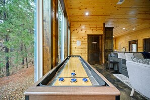 Una mesa de shuffleboard con tres discos, un sofá y una puerta que indica 'Lounge Room' en un interior de madera.