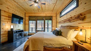 A wooden cabin bedroom with a bed, a TV, and a fireplace. - Moonshine Times - great outdoor space, hot tub, playground, firepit (Broken Bow)