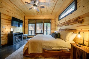Un dormitorio tipo cabaña de madera con cama, televisor y chimenea.